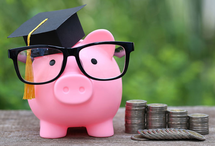 piggy bank wearing glasses and a gradtuation cap with stacks of coins beside it